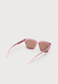 Óculos de sol retangulares cor de rosa com lentes castanhas. Armação transparente, textura suave e hastes finas. Apresenta uma marca discreta na lateral.