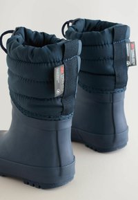 Marinblå vattentäta stövlar med vadderad topp, elastisk snodd och texturerade gummisulor. Har en 3M-isoleringstags på sidan.