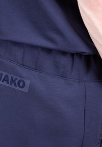 Pantalons de sport bleu marine en tissu doux, dotés d'une taille élastique et d'un logo JAKO dans une couleur contrastante le long de la couture latérale.