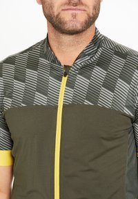 Maillot de cyclisme à manches courtes en vert foncé avec un motif géométrique gris, fermeture éclair jaune et accent jaune contrastant sur les manches.