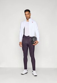 Dviračių apranga, kurią sudaro balta lengvo svorio striukė, juodos bib tamprės su logotipu ir juoda šalmas, balti dviračių batai.