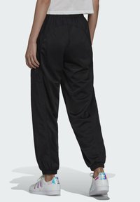 Svarta träningsbyxor med resårmidja, med en slät textur och avsmalnande ben. Bärs med vita sneakers som har en blanka, iriserande häl.