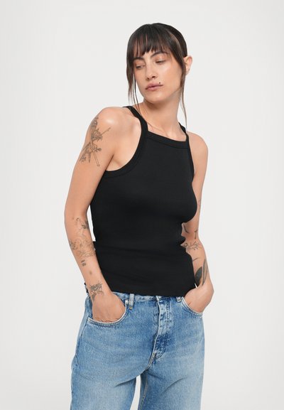 Top de alças pretas caneladas com decote quadrado e alças finas, combinado com jeans de ganga de cintura alta, azul claro.