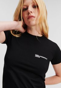 T-shirt in cotone nero a maniche corte, con logo bianco ricamato "KARL LAGERFELD JEANS" sul lato sinistro del petto. Tessuto morbido, design aderente.