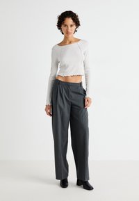 Top cropped blanc à côtes avec un ourlet en dentelle, associé à un pantalon gris taille haute plissé. Le modèle porte des chaussures à talons carrés noires.