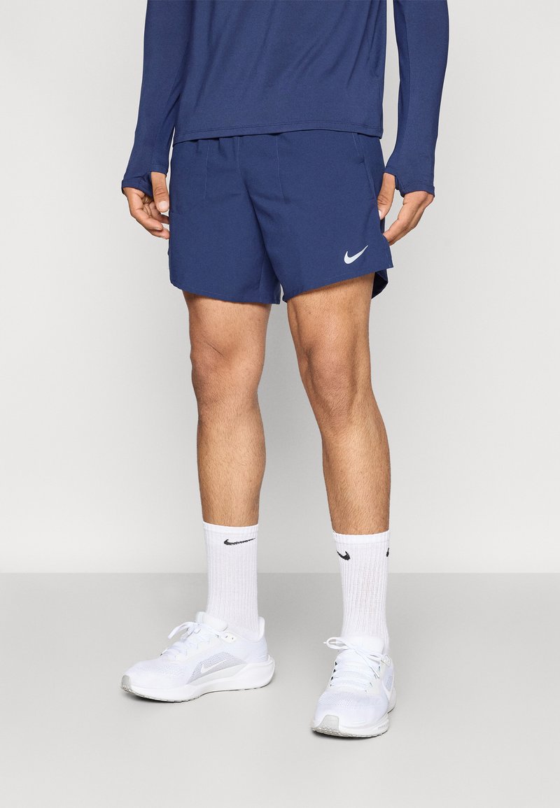 Σκούρο μπλε σορτς Nike με απαλή υφή, εφαρμοστή σχεδίαση και λευκό λογότυπο Nike. Συνδυασμένα με λευκά αθλητικά παπούτσια και κάλτσες.