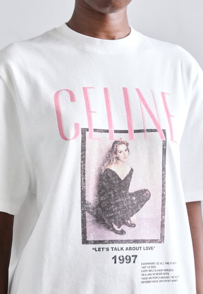 T-shirt en coton blanc avec un imprimé graphique vintage mettant en avant le mot "CELINE" en rose, un portrait et du texte en noir. Manches courtes, col rond.