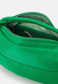 Borsa in tessuto verde brillante con due cerniere argentate aperte che mostrano un interno grigio chiaro e una piccola tasca con cerniera all'interno.
