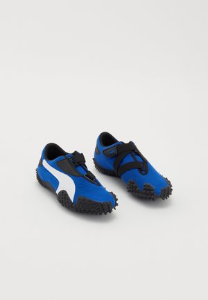 Siniset urheilusandaalit, joissa valkoinen korostus, kangasilmeinen yläosa, teksturoitu musta kumipohja ja joustava hihna. Kevyt ja minimalistinen muotoilu.