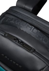 Sac à dos noir en matériau durable, avec des fermetures éclair texturées et des accents contrastants de couleur aqua. Marquage en relief notable sur les sangles.