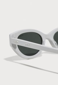 Valged cat-eye prillid roheliste läätsedega, mille templitel on Swarovski kristallide aktsent. Valmistatud läikivast plastmaterjalist, millel on sile tekstuur.