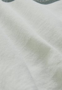 Tessuto bianco con una superficie morbida e testurizzata, caratterizzato da leggere pieghe e grinze per un aspetto rilassato. Nessun motivo o accento visibile.