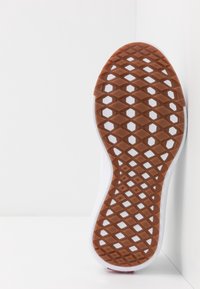 Weißer Sportschuhsohle mit einer strukturierten braunen Gummifläche, die ein Wabenmuster aufweist. Abgerundete Kanten mit einem klaren Design.