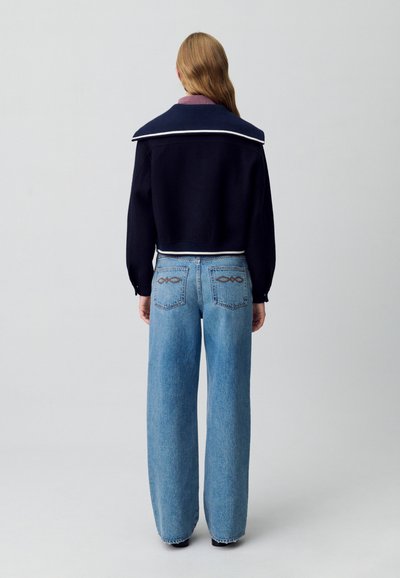 Suéter recortado azul marino con un cuello blanco en contraste, combinado con jeans de pierna ancha azul claro que presentan costuras decorativas en los bolsillos traseros.