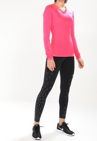 Long-sleeve bright pink athletic top paired with black leggings featuring diagonal white lines. Both made from flexible, moisture-wicking material.