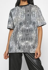 Koszulka z krótkim rękawem w czarno-białym wzorze węża, z okrągłym dekoltem. Charakteryzuje się luźnym krojem i gładką fakturą.