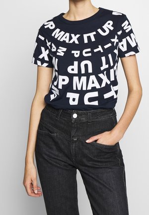 Osoba nosząca granatowy T-shirt z rozproszonymi białymi literami tworzącymi frazę "MAX IT UP" w połączeniu z czarnymi, wysokim stanem jeansami.