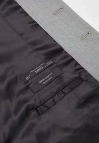 Vnitřek šedého saka má hladkou černou podšívku, štítky "Super Slim Fit" a "Stretch Fabric" a šedou vnější látku s kovovými prvky.
