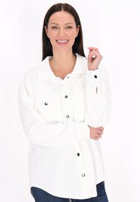 Giacca bianca a camicia con un motivo a spina di pesce testurizzato, tasche sul petto e chiusura a bottoni a pressione, con maniche lunghe.