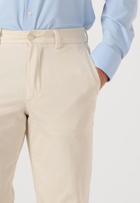 Beige chino's met een gladde textuur, voorzien van een enkele knoopsluiting, twee zijzakken en een rechte pijp, gecombineerd met een lichtblauw shirt.