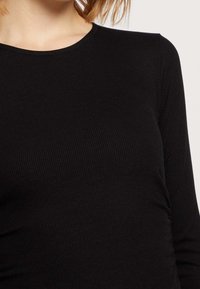 Svart ribbad långärmad tröja med rundad halsringning, med subtila volangdetaljer på sidorna och en tajt passform.