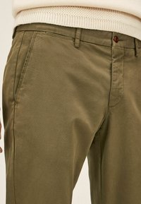 Olivgrüne Chinos aus einem Baumwollmischgewebe, mit geradem Schnitt, seitlichen Taschen und einem einzelnen Knopf vorne.