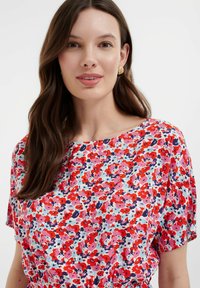 Blumenshirt mit einem hellen, mehrfarbigen Muster in Rot-, Pink- und Blautönen. Aus weichem Stoff, mit rundem Ausschnitt und lockeren Ärmeln.