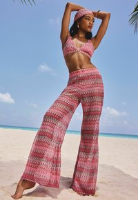 Roze, bedrukt twee-delig ensemble bestaande uit een bralette-top en flared broek met golvende lijnen in donkere tinten, gemaakt van lichte stof.