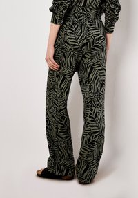 Palazzo pants in olive green with a black zebra leaf pattern. Loose fit, elastic waistband, lightweight fabric, and flared legs.