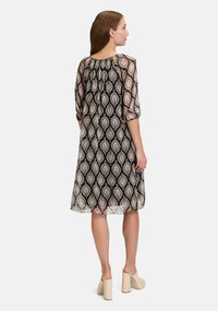 Schwarz- und cremefarbenes gemustertes Kleid mit Dreiviertelärmeln, gerafftem Ausschnitt und leichtem, fließendem Stoff. Mittellanges Design.