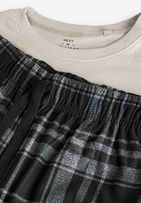 Graues Crew-Neck-T-Shirt, das über schwarzen und grauen Karo-Schlafanzughosen mit elastischem Bund und Kordelzugdetail getragen wird. Weicher Stoff.