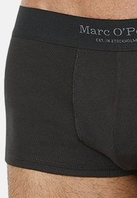 Schwarze Boxer-Shorts mit gerippter Textur, ausgestattet mit einem einfarbigen Bund, auf dem "Marc O’Polo" in Grau geprägt ist.