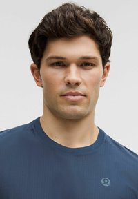 Camiseta atlética azul marino con cuello redondo, que presenta un logo sutil en el lado izquierdo, fabricada con una tela suave y ligera.