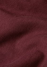 Tela de punto burdeos con una superficie suave y texturizada, que presenta un patrón de tejido fino y uniforme y un brillo sutil, adecuada para ropa o tapicería.