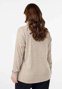 Bežani pleteni pulover s teksturiranim uzorkom pletenice, dugim rukavima i okruglim izrezom. Donji rub je blago zakrivljen.