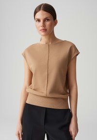 Beige, gebreide top met korte mouwen, een ronde halslijn en een middennaad; losse pasvorm en geribbelde zoom, gecombineerd met zwarte broek.