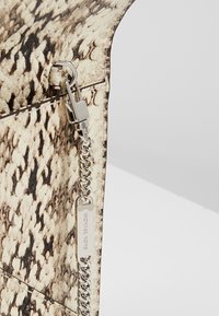 Sac à main à motif peau de serpent en beige et marron avec une chaîne argentée et une fermeture à clip, présentant une surface texturée et détaillée.