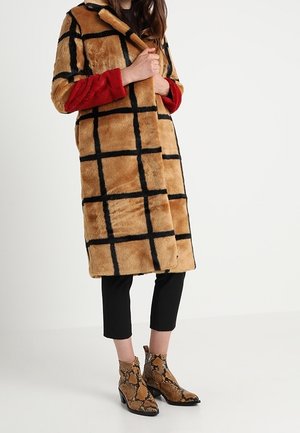 Person wearing a long tan and black checkered faux fur coat, red sleeves, black cropped pants, and snakeskin-patterned ankle boots.