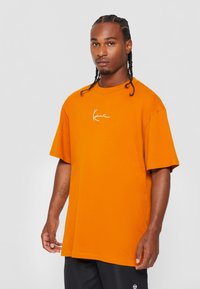 Tricou din bumbac portocaliu, cu mâneci scurte și gât rotund. Prezintă un logo scriptat alb pe piept. Design lejer.