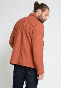 Braune Lederjacke mit klassischem Kragen und gesteppten Paneeldetails, kombiniert mit dunkelblauen Jeans. Strukturierten Oberfläche, lockere Passform.