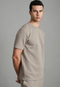 Tricou scurt cu mânecă scurtă, de culoare bej deschis, fabricat dintr-un material moale. Dispune de un guler rotund și o croială lejeră. Design curat, minimalist, cu umeri fără cusături.