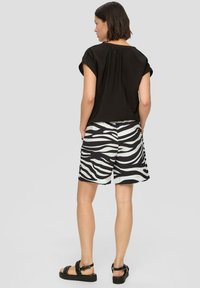 Czarny krótki top z krótkim rękawem o teksturowanym wykończeniu, zestawiony z krótkimi spodniami w zebra w czerni i bieli, noszonymi z czarnymi sandałami.