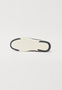 Semelle de chaussure avec une base en caoutchouc blanc texturé et un accent noir. Présente un motif en vagues sur la zone blanche pour une meilleure adhérence.