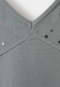 Tissu tricoté gris avec un décolleté en V et de petits sequins ronds dispersés près du décolleté sur un vêtement.