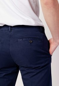 Chinos blu navy con una texture liscia e tasca posteriore con bottone, abbinati a una camicia bianca aderente.