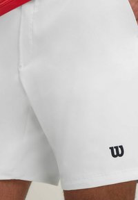 Weiße Sportshorts mit glatter Textur, versehen mit einem schwarzen "W"-Logo am Unterschenkel und einem seitlichen Taschendetail.