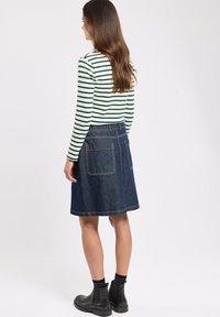 Haut à manches longues rayé et jupe en denim avec poches arrière. La jupe est bleu foncé avec des coutures visibles ; des bottines complètent la tenue.