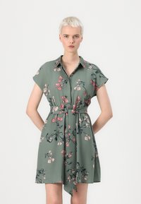 Abito floreale verde con maniche corte, un davanti con bottoni e vita con cintura. Presenta motivi floreali rosa e blu scuro. Tessuto morbido al tatto.