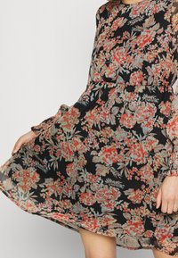 Schwarzes Blumenkleid mit einer Mischung aus roten und blauen Blumen. Hergestellt aus leichtem Stoff, mit langen Ärmeln und einem plissierten Rockdesign.