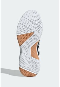 Semelle de sneaker texturée blanche et beige avec des motifs de grip circulaires et ovales, avec un petit logo triangulaire près du centre.